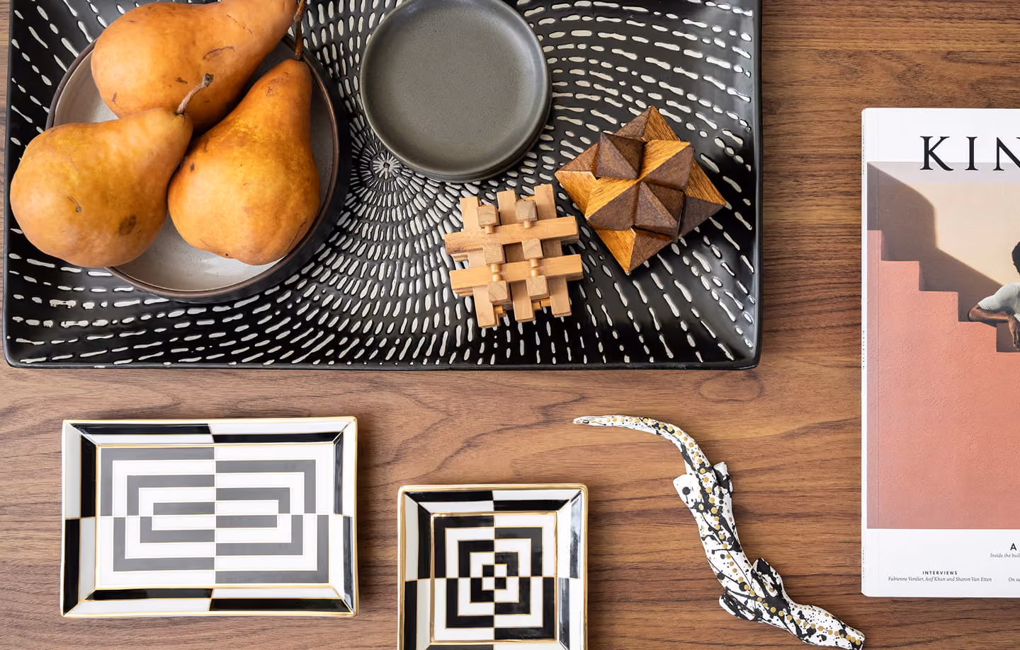 Wooden table with a black patterned tray holding pears, plates, wooden puzzles, and a magazine.