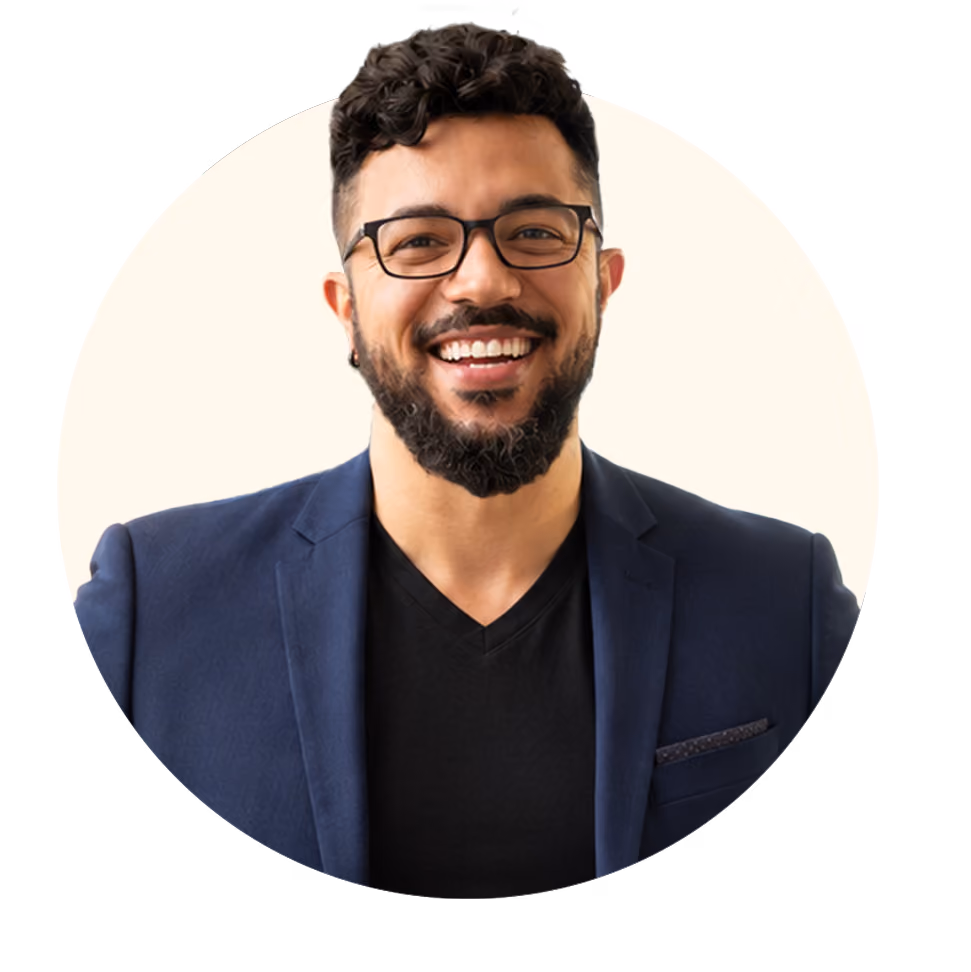 Smiling man with beard and glasses wearing a blue blazer and black shirt.