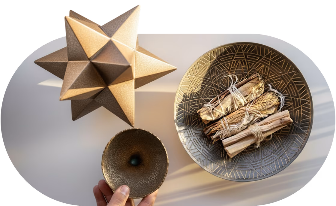 Hand holds a small bronze bowl next to decorative bronze star and bowl with tied wood bundles.