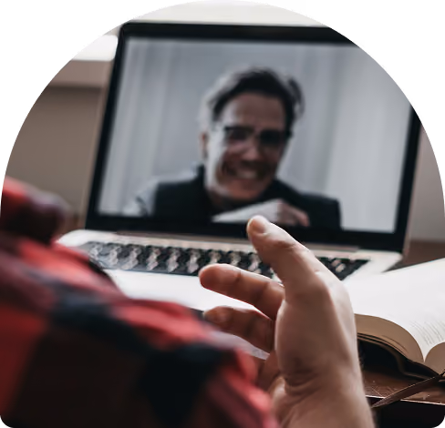 Person gesturing with hand during a video call on a laptop, with an open book nearby.