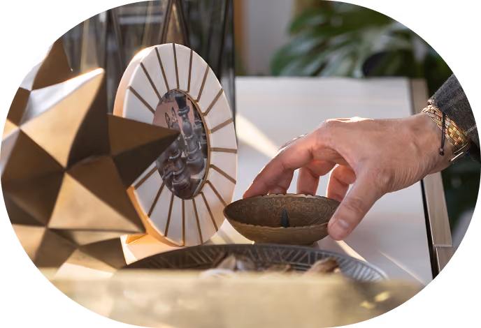 Hand holding a small decorative brass bowl near geometric and circular sculptures on a table.