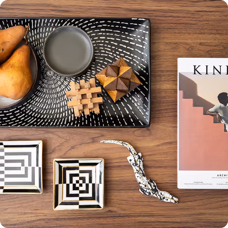 Black tray with pears, wooden puzzles, two patterned square dishes, ceramic lizard, and a Kinfolk magazine on wood table.