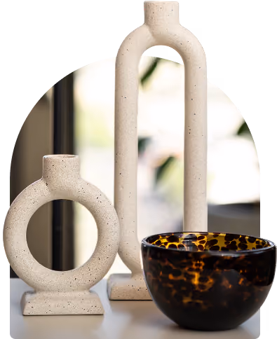 Two textured beige stone vases and one tortoiseshell-patterned glass bowl on a surface.