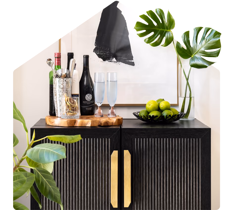 Black cabinet with gold handles holds wine bottles, glasses, green limes, and leaf decor in vases.