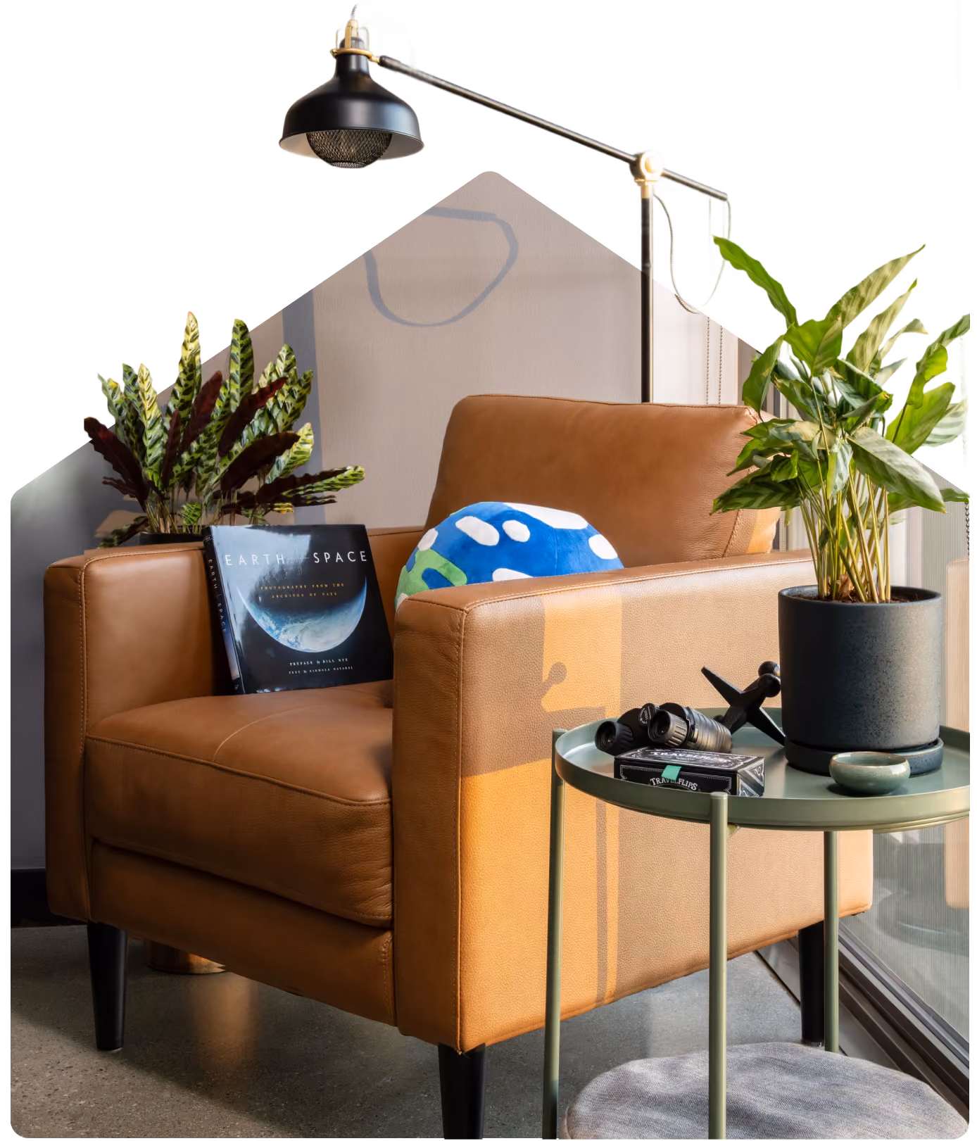 Brown leather armchair with Earth book and globe pillow beside a green side table with plants and binoculars.