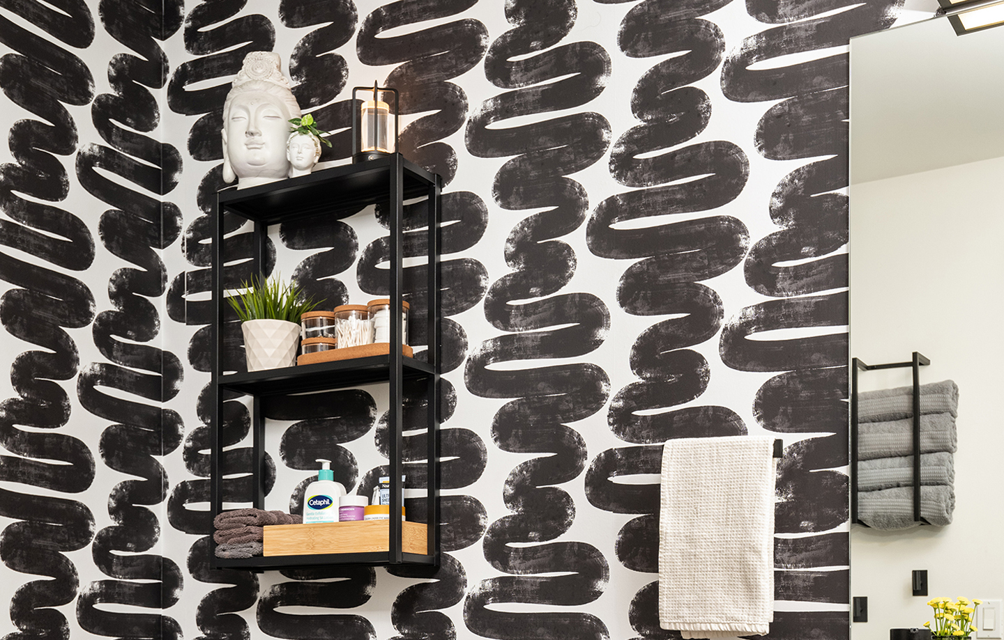 Bathroom wall with black abstract brushstroke pattern, black shelf holding decor, towels on racks.