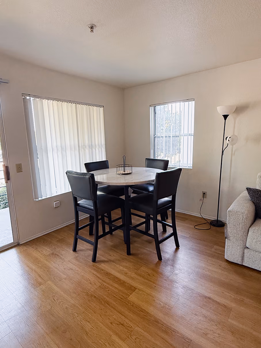 Dining nook with a round counter-height marble table and four black leather barstools beside two bright windows