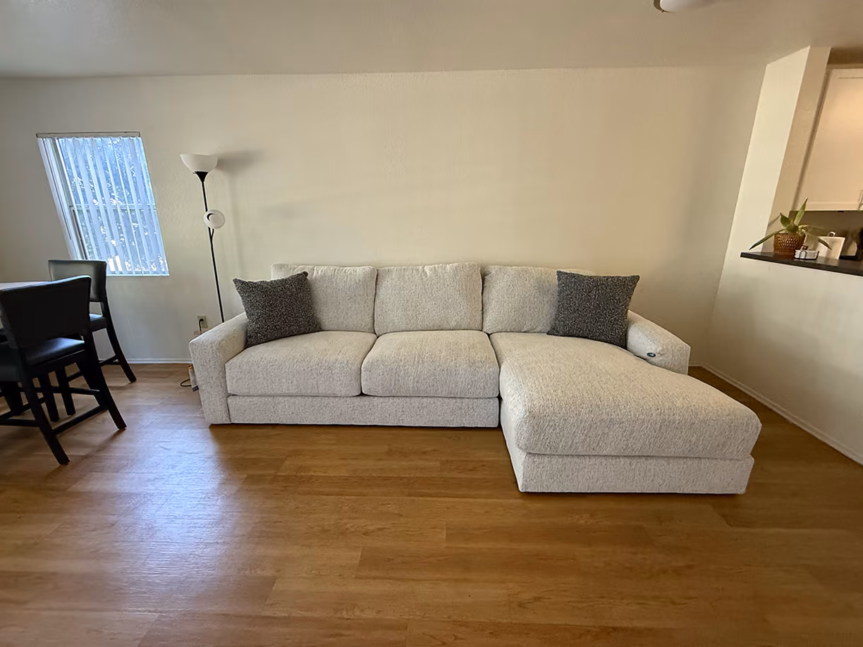 Cream chenille sectional sofa with a chaise and charcoal throw pillows in an open living room with wood floors