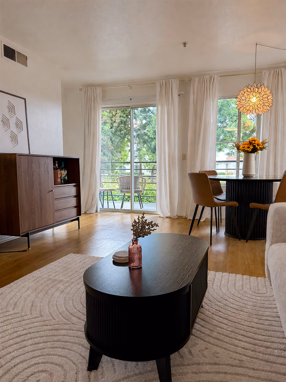 Styled living room with an oval black coffee table, textured cream rug, walnut bar cabinet, and fluted black dining table