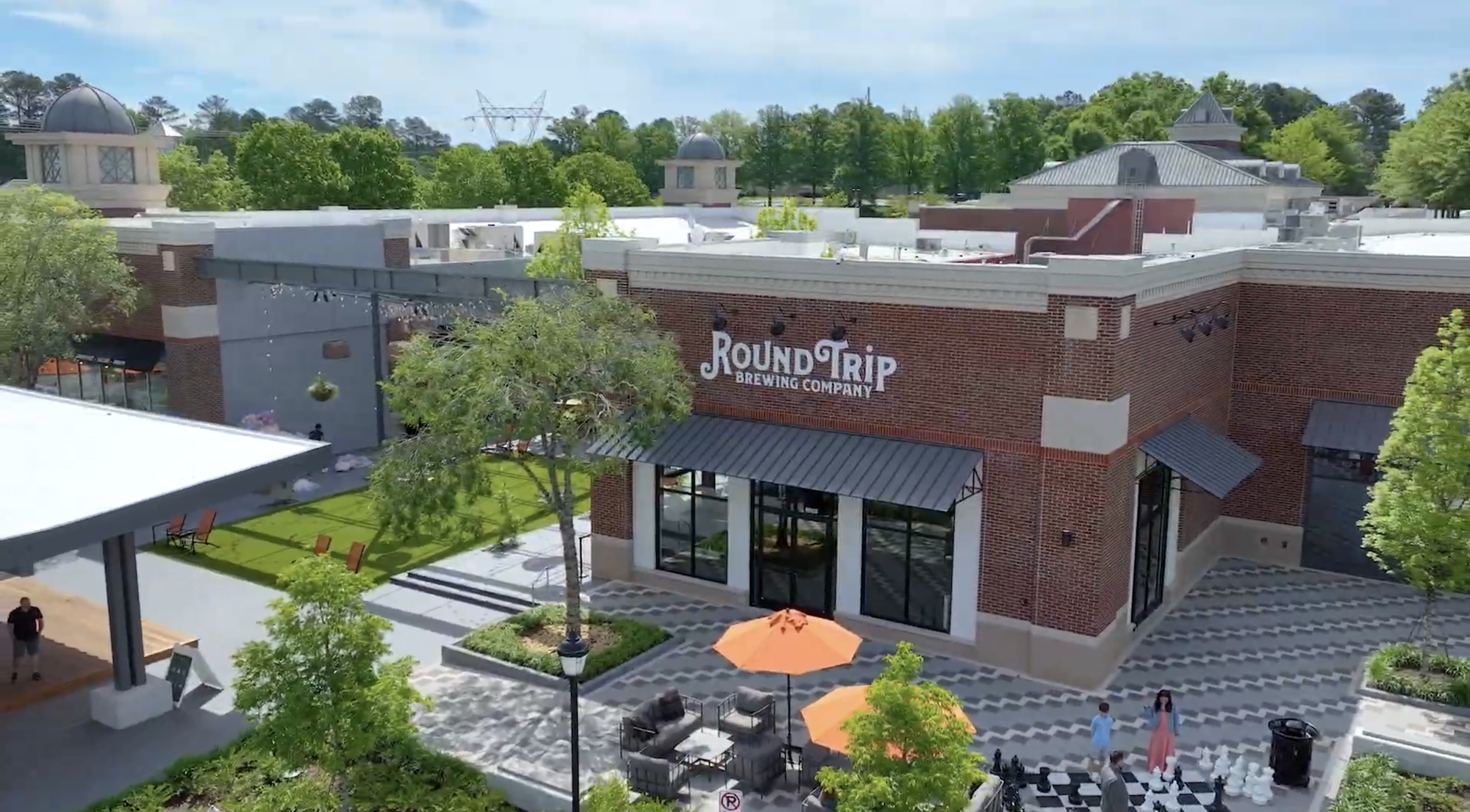 Outdoor view of Round Trip Brewing Company with patio seating, orange umbrellas, trees, and people playing giant chess.