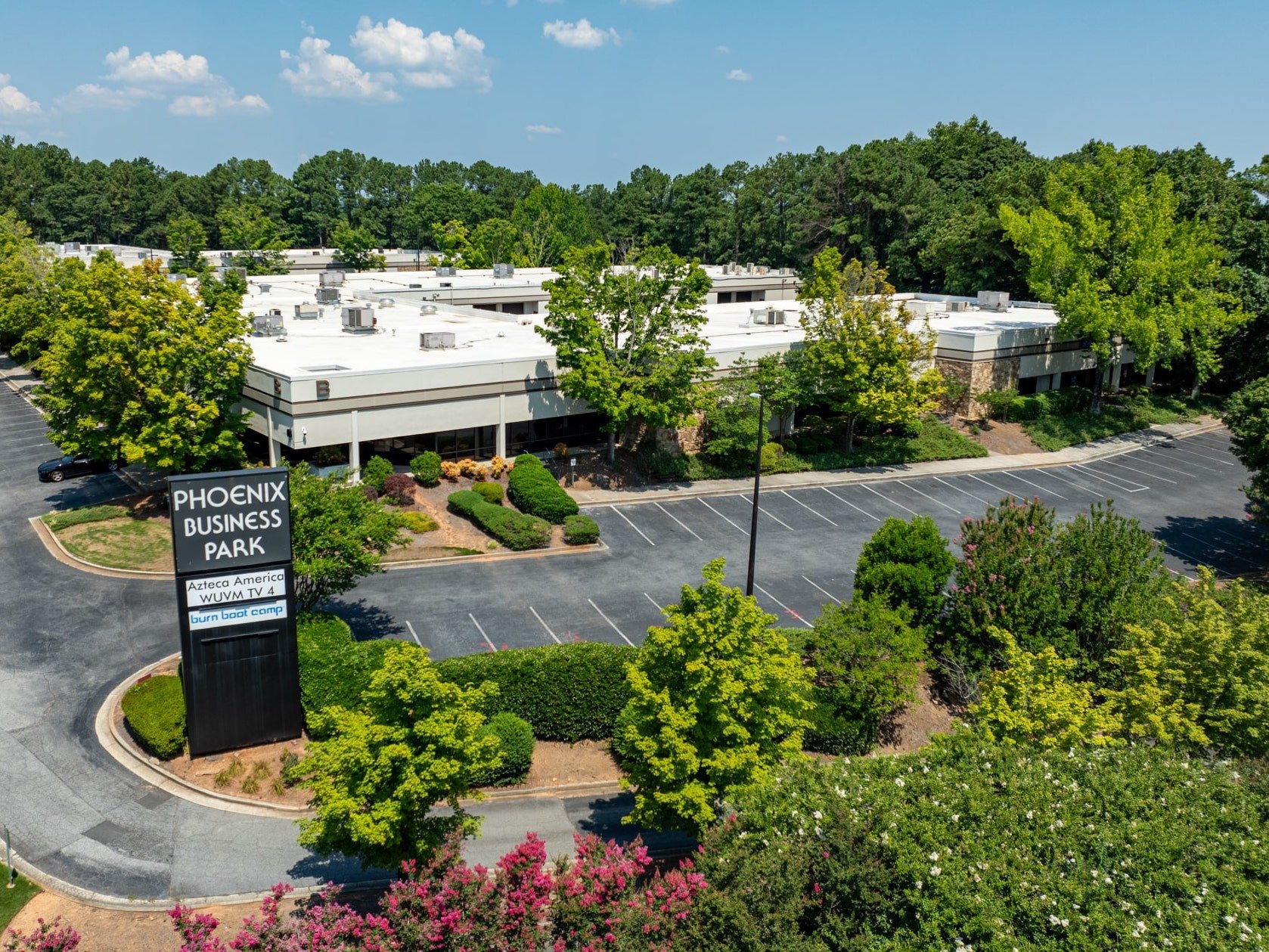 Aerial view of Phoenix Business Park with office buildings surrounded by trees, landscaping, and empty parking lots under a clear blue sky.