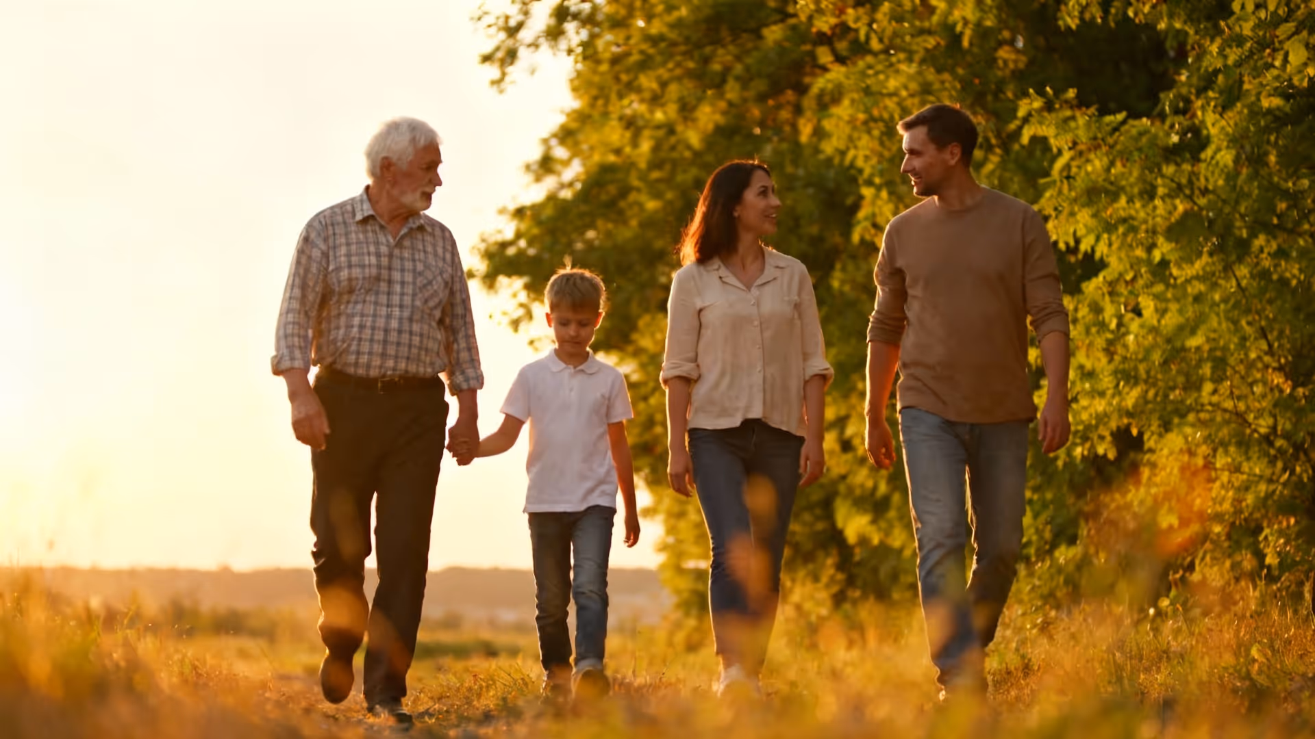 Family of four walking outdoors on a path surrounded by greenery during golden hour.