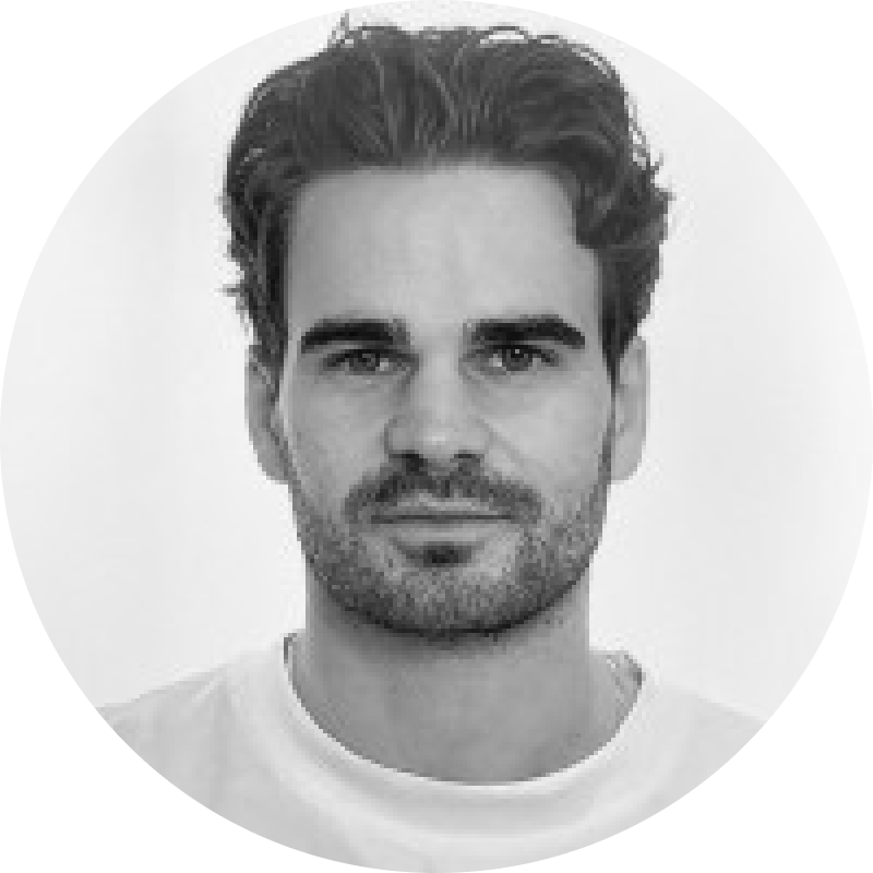 Black and white close-up portrait of a man with short wavy hair, beard, and a neutral expression, wearing a light-colored shirt.
