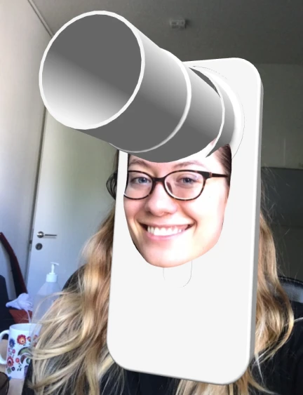 Person smiling with glasses and long hair, their face digitally inserted into a white device resembling a large telescope on a smartphone-shaped base.