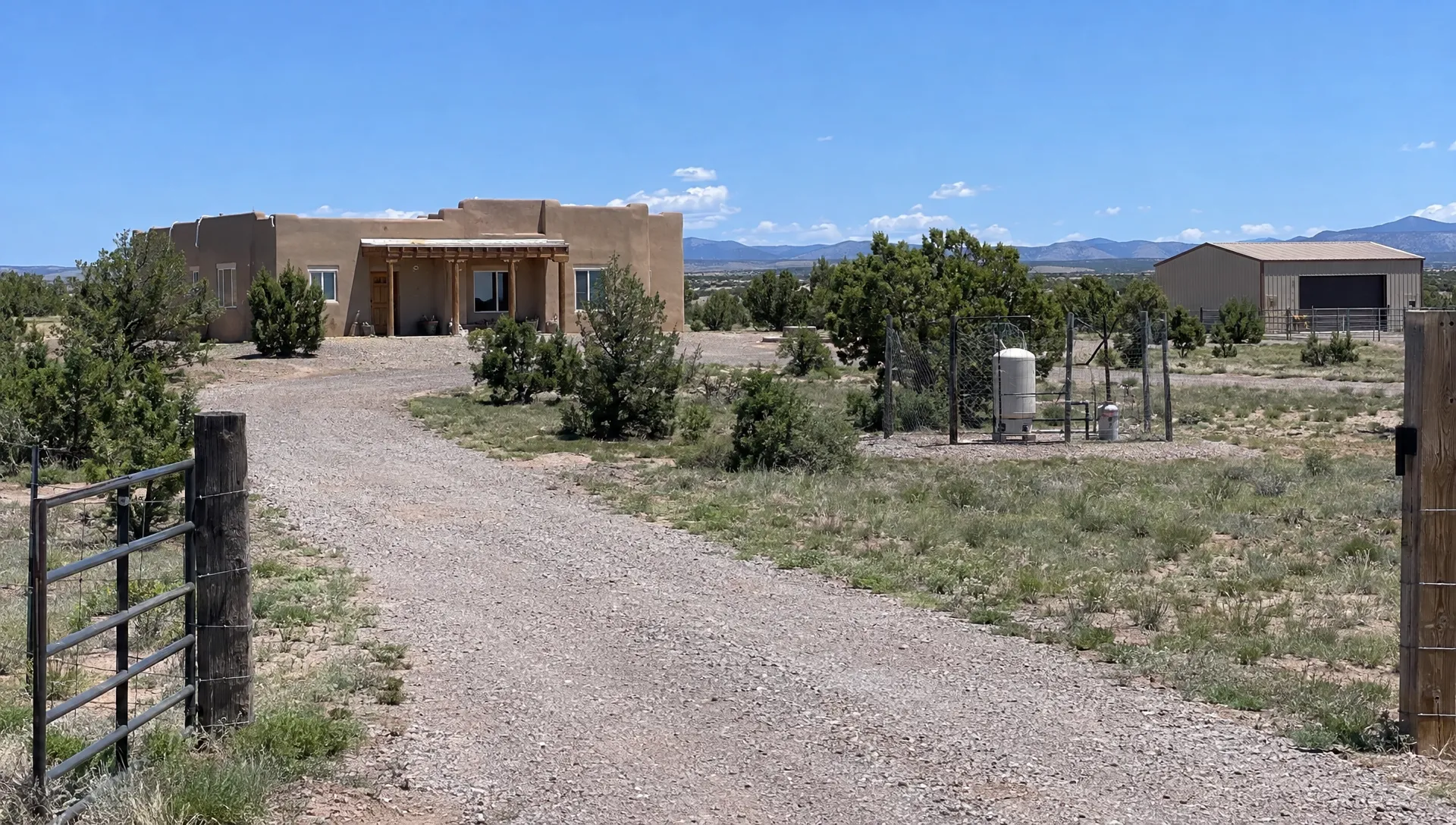 An adobe home, gravel access road, fenced well enclosure, and detached barn show features to review for New Mexico home loans.