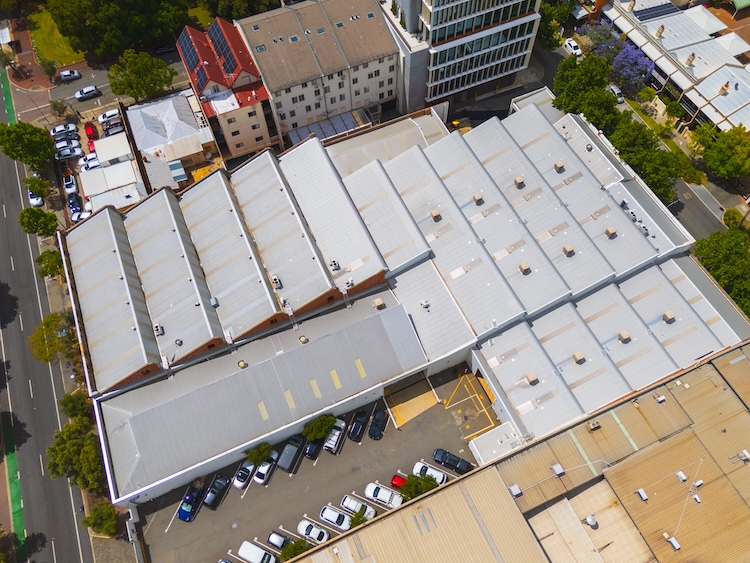 Aerial view of large industrial buildings with multiple peaked roofs and parking lot with cars surrounding the complex.