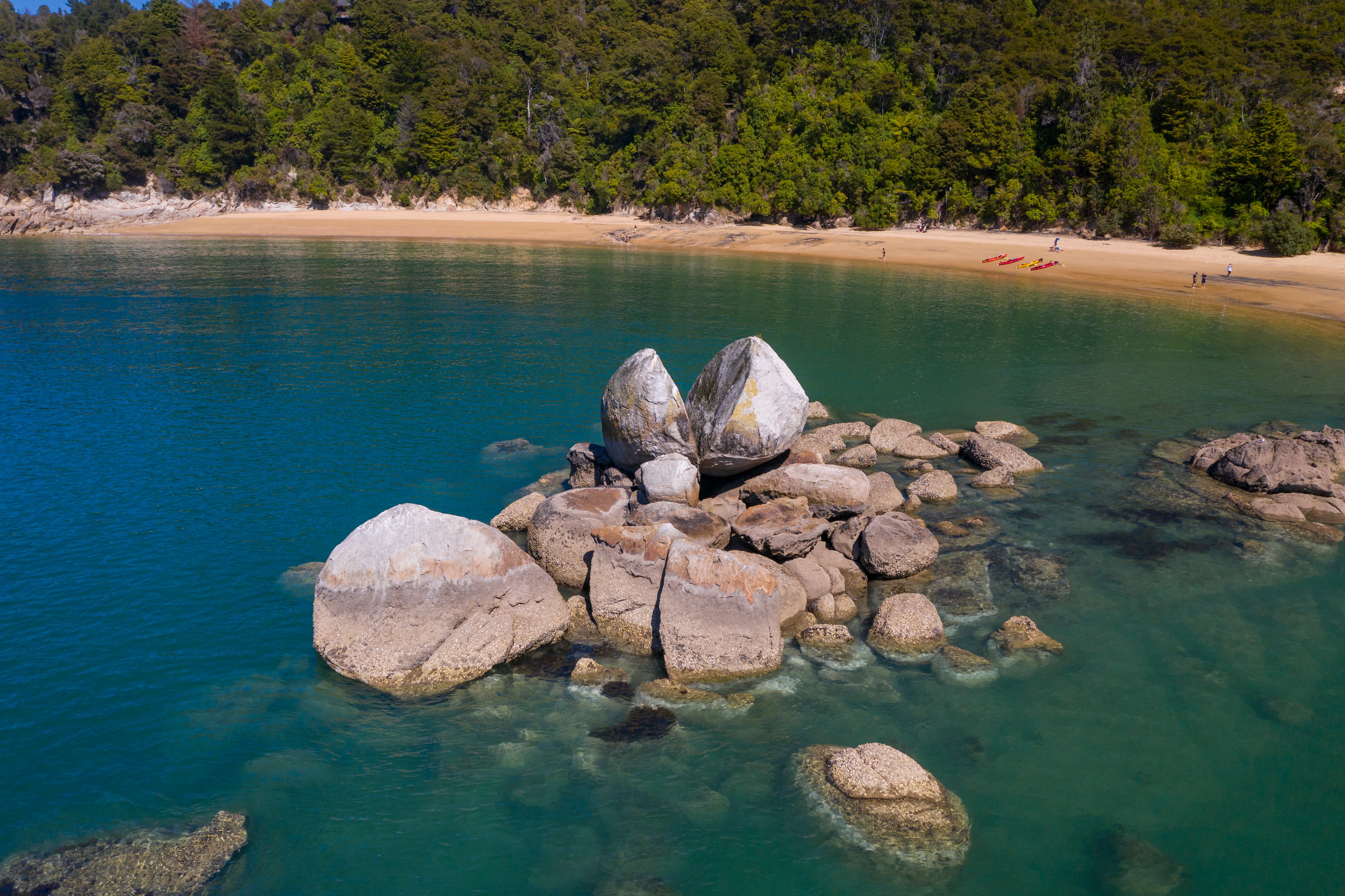 Split Apple Rock, a large split boulder formation in clear blue water near a sandy beach and forest.