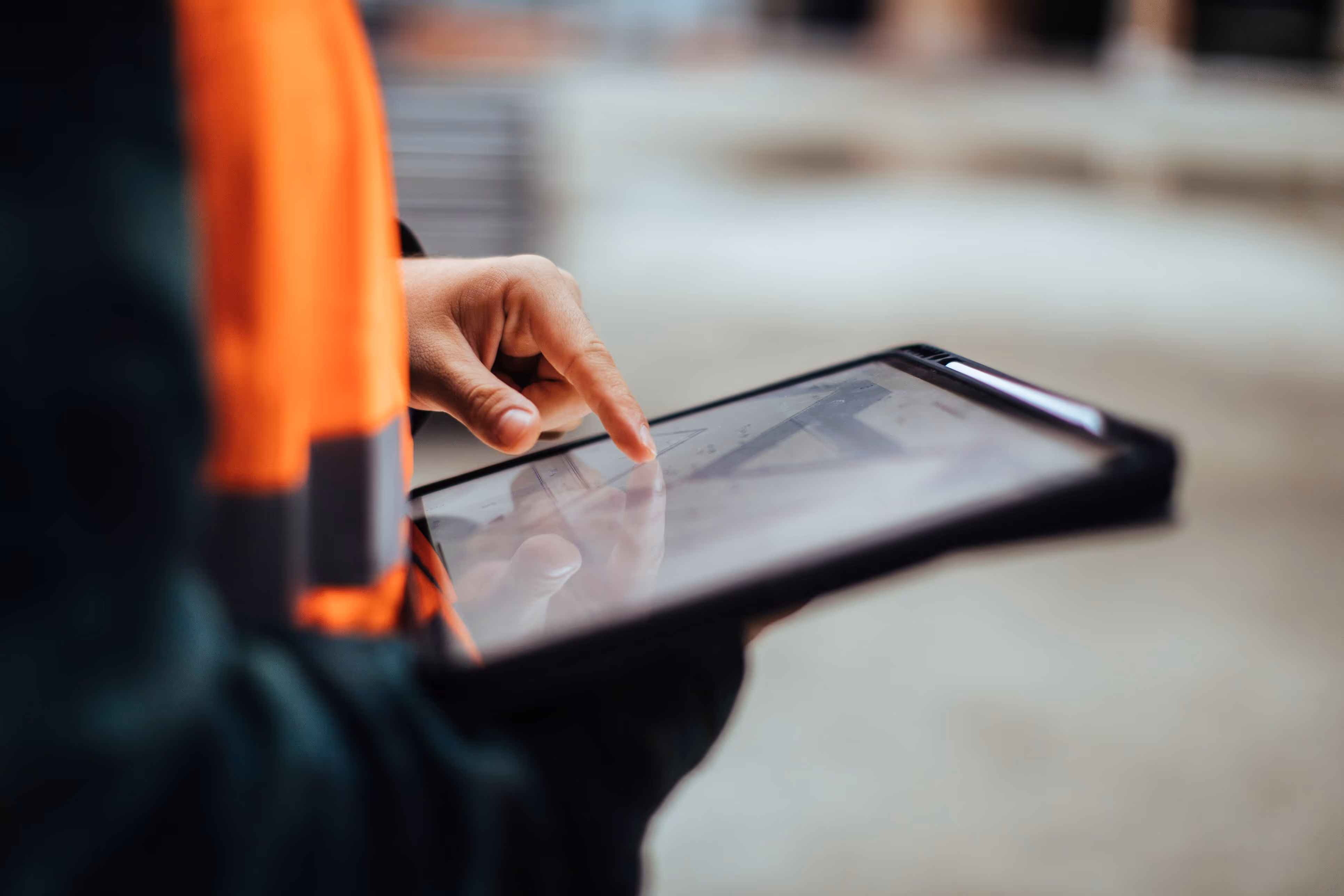 Person in an orange safety vest using a tablet with architectural or construction plans displayed.