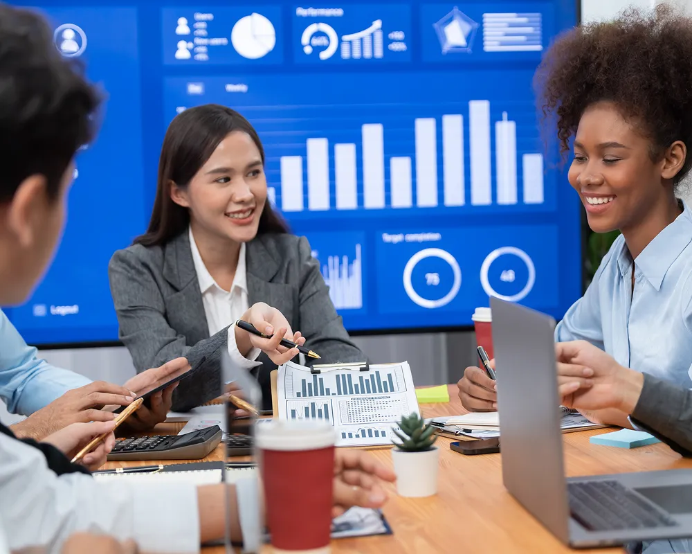 Business team discussing charts and data during a meeting with graphs displayed on a screen.