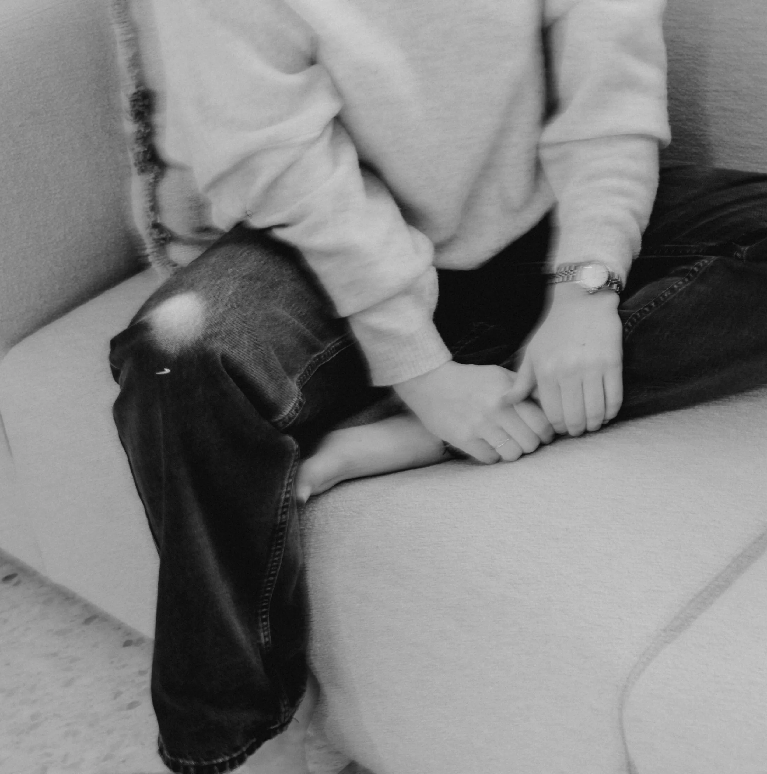 Persoon zittend gekruist met een trui, spijkerbroek met een gat in de knie en een horloge.