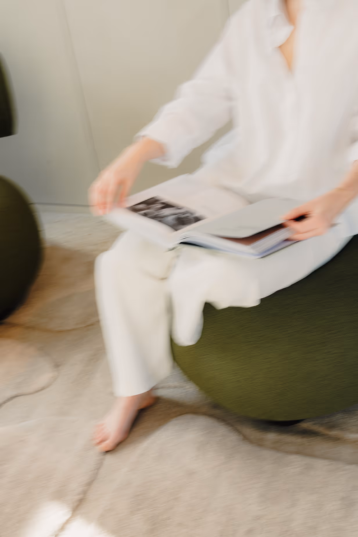 Onscherpe afbeelding van een persoon in witte kleding die op een groene stoel zit en een open boek vasthoudt.