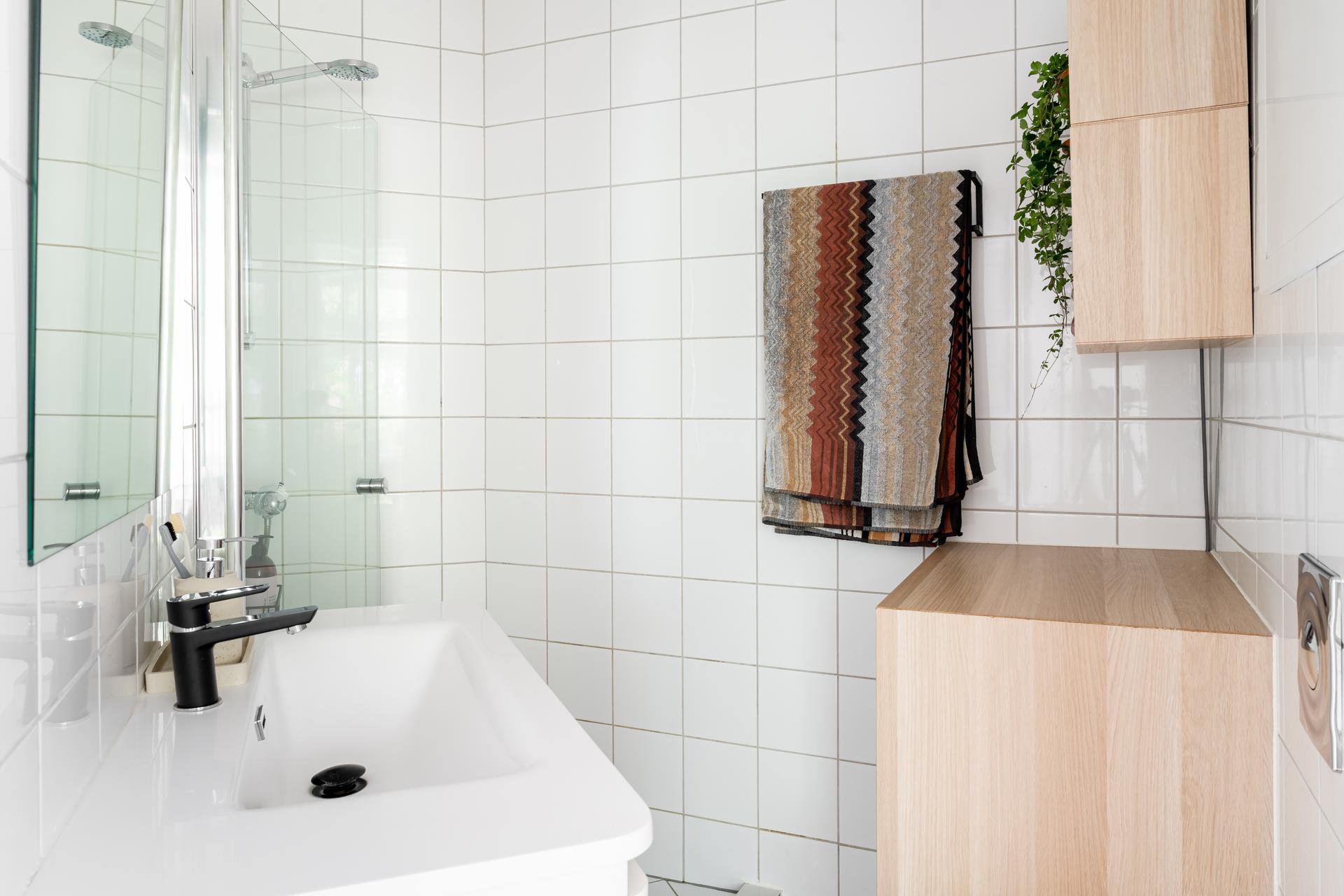 Badet inneholder vegghengt toalett, dusjdører i glass og opplegg for vaskemaskin.
