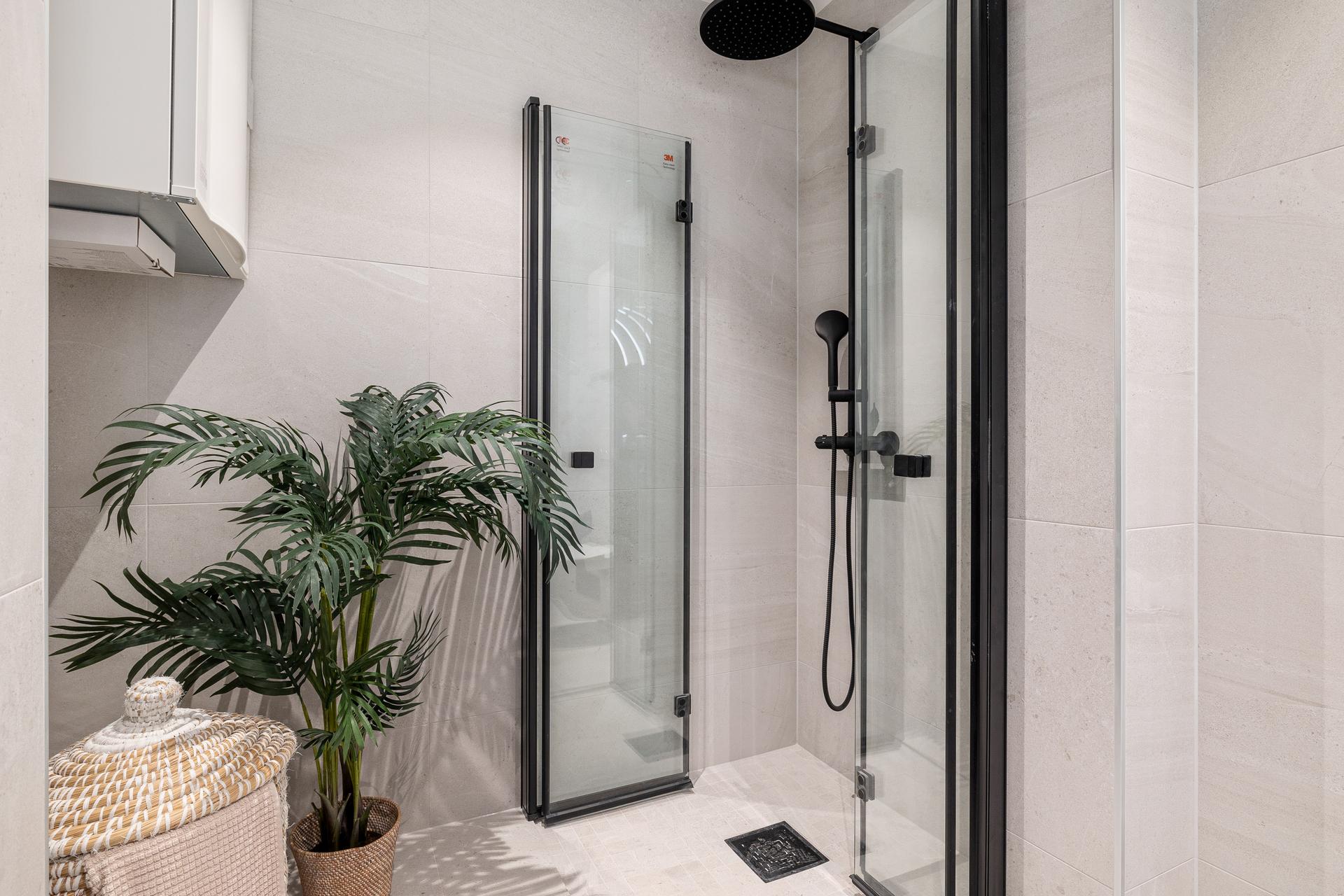 Badet inneholder vegghengt toalett, helstøpt servant med skuffer under, dusjdører i klart glass og opplegg for vaskemaskin. 