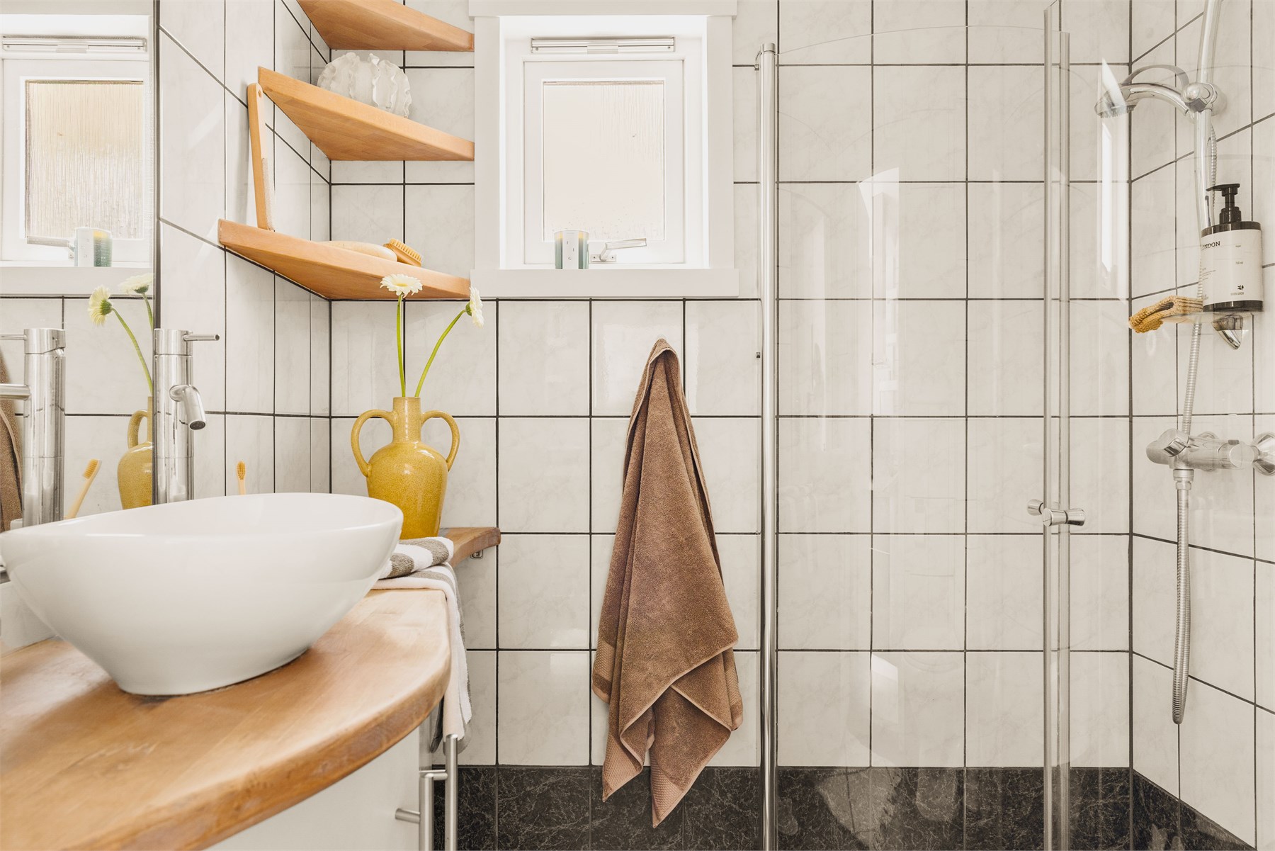 Badet inneholder toalett, helstøpt servant med skap under og dusjdører i klart glass. 