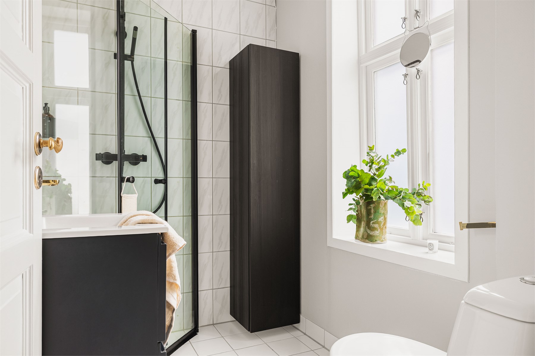 Badet inneholder toalett, helstøpt servant med skuffer under og dusjdører i klart glass. 