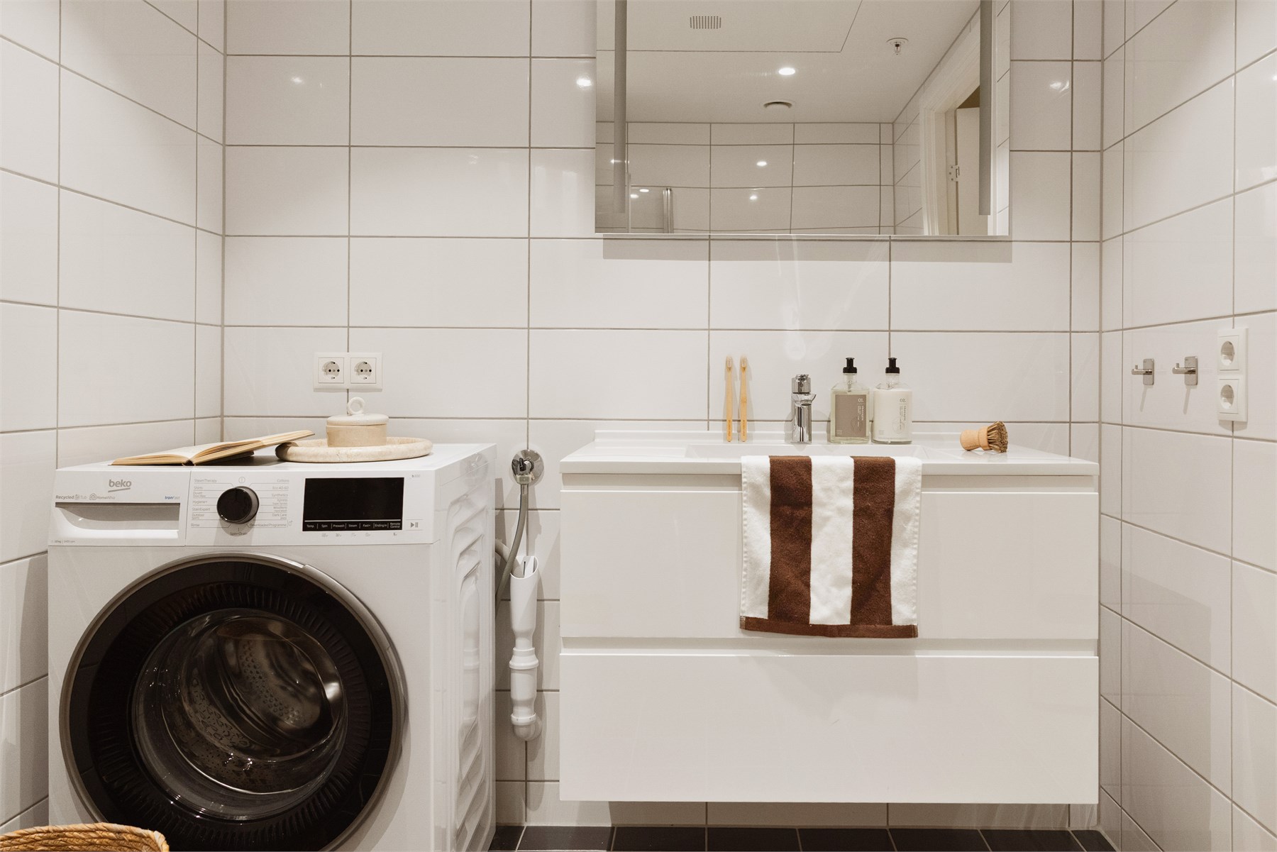 Badet har en praktisk og gjennomtenkt innredning med servant og tilhørende møblement, speil og belysning, vegghengt wc samt dusjnisje med foldedører. Det er også opplegg for vaskemaskin og tørketrommel. 