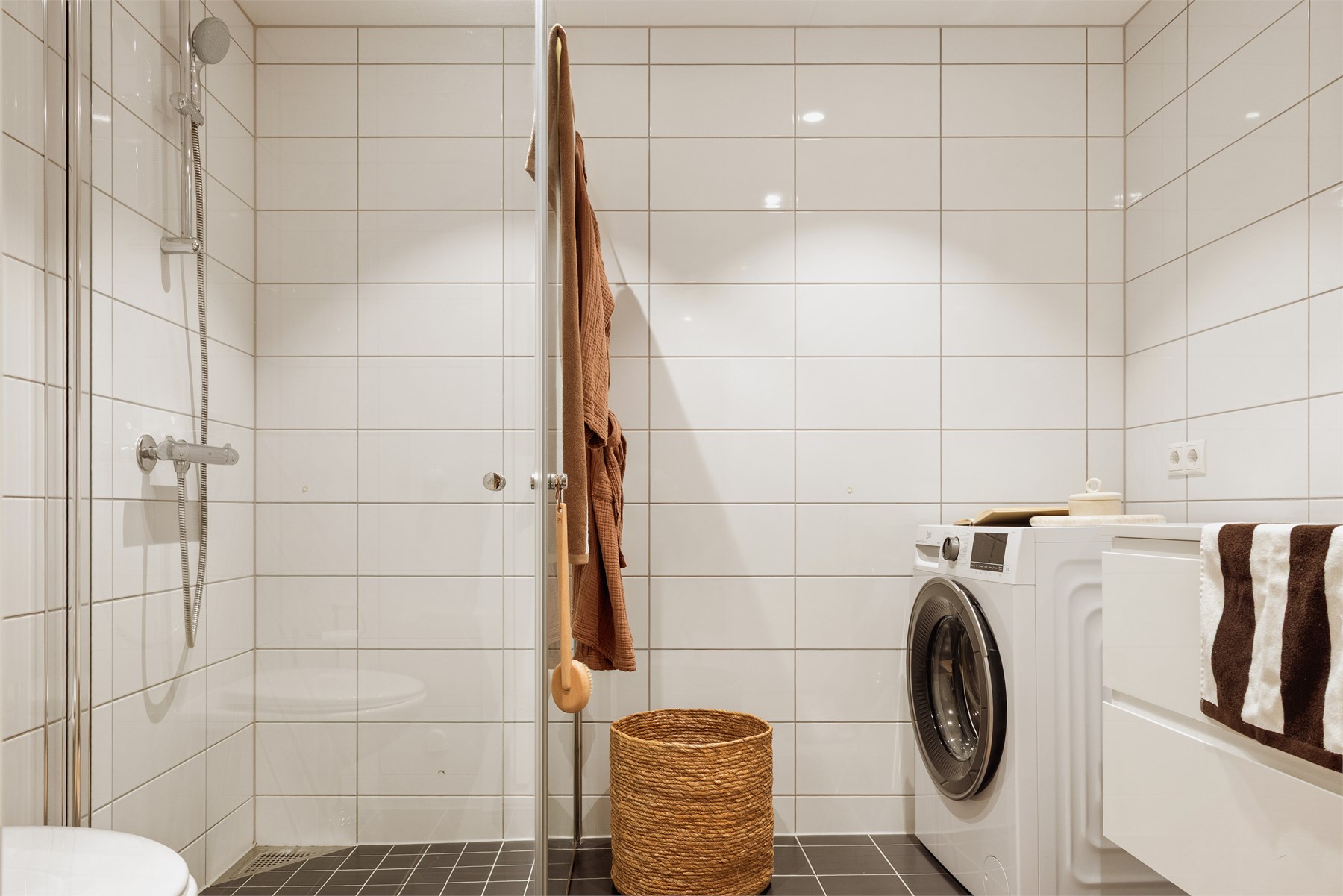 Badet har et pent og moderne uttrykk med helflisede overflater, downlights i tak og vannbåren gulvvarme som sørger for god komfort. Videre er rommet utstyrt med avtrekk til boligens balanserte ventilasjonsanlegg og rør-i-rør-system.