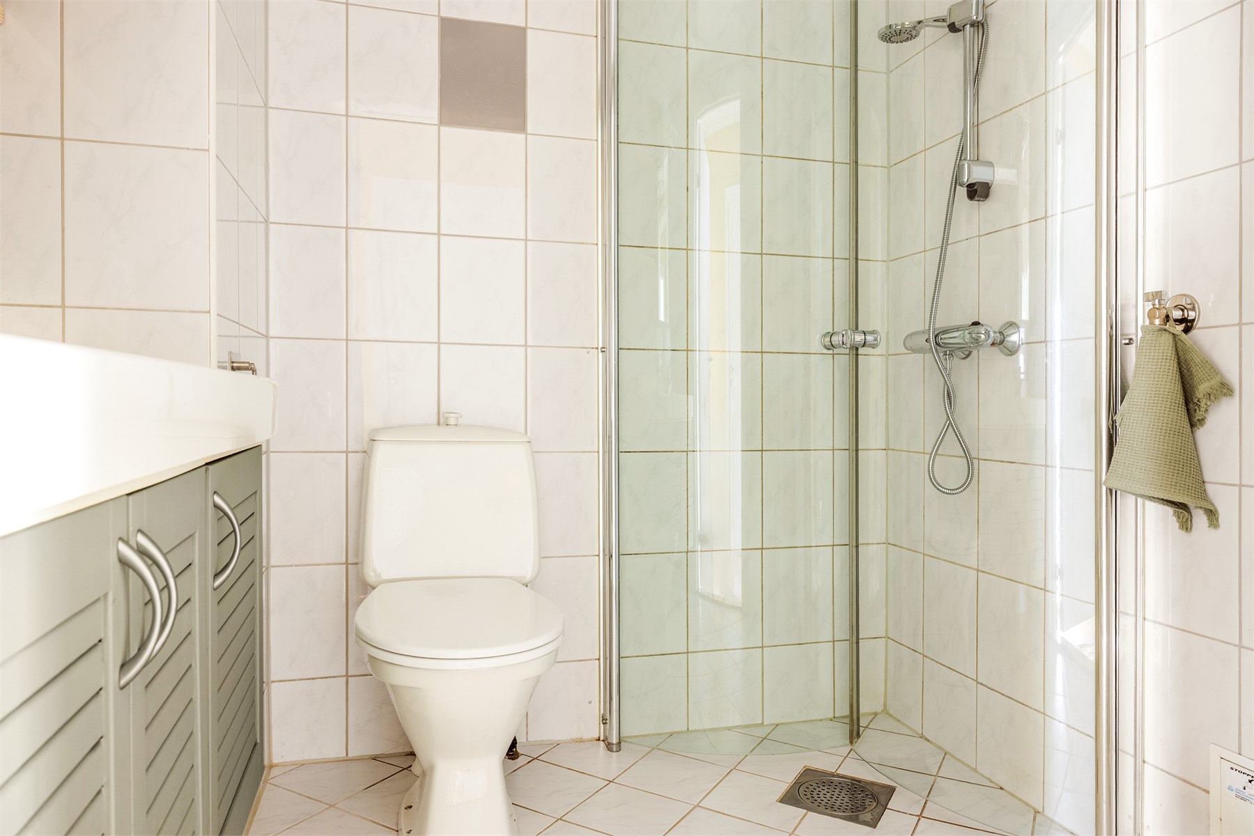 Badet inneholder toalett, helstøpt servant med skap under og dusjdører i klart glass.