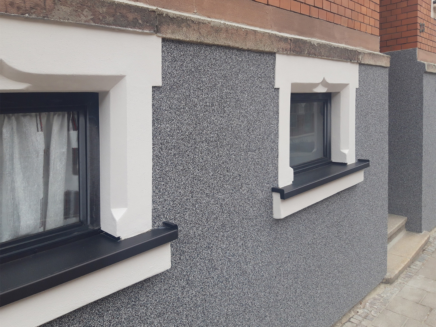 Detailansicht eines Haussockels: Strapazierfähiger Buntsteinputz in Grau schützt die Fassade effektiv vor Spritzwasser und Schmutz.