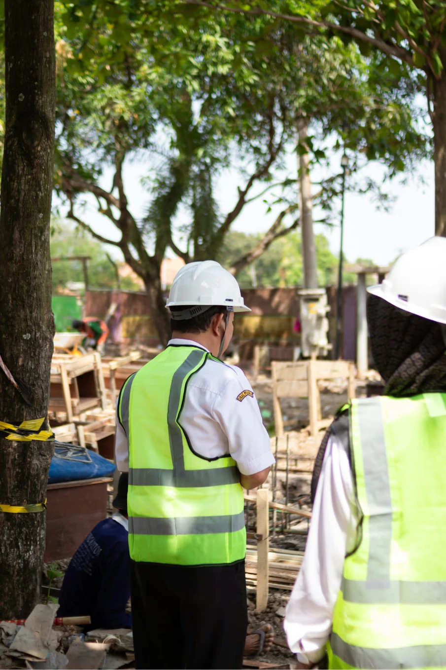Deux agents de sécurité portant des gilets jaunes réfléchissants et des casques blancs sur un chantier extérieur.