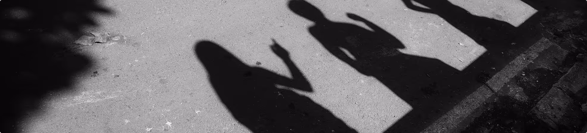 Shadows of three people on pavement with two raising their hands.