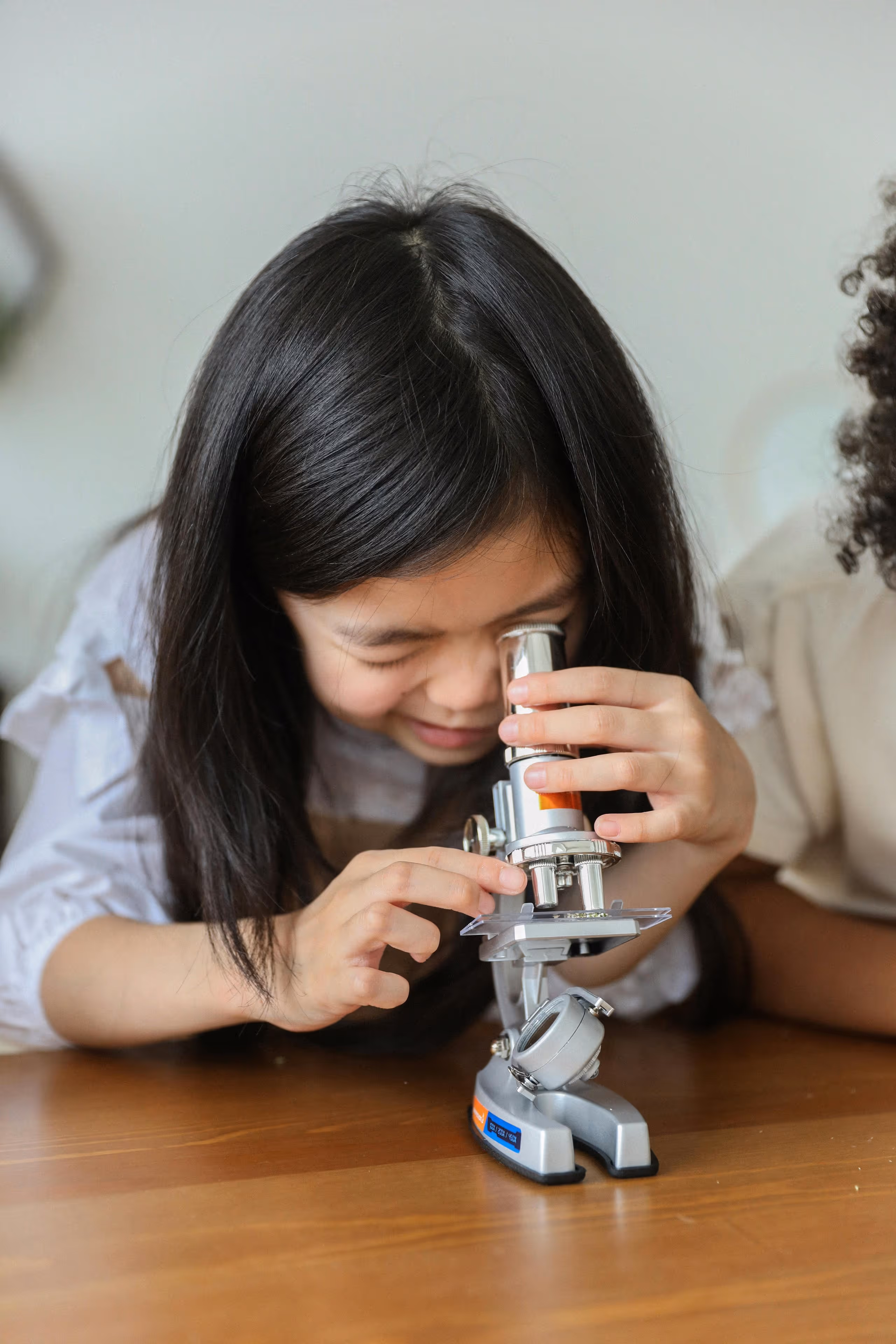 Young girl looking through a microscope on a wooden table.