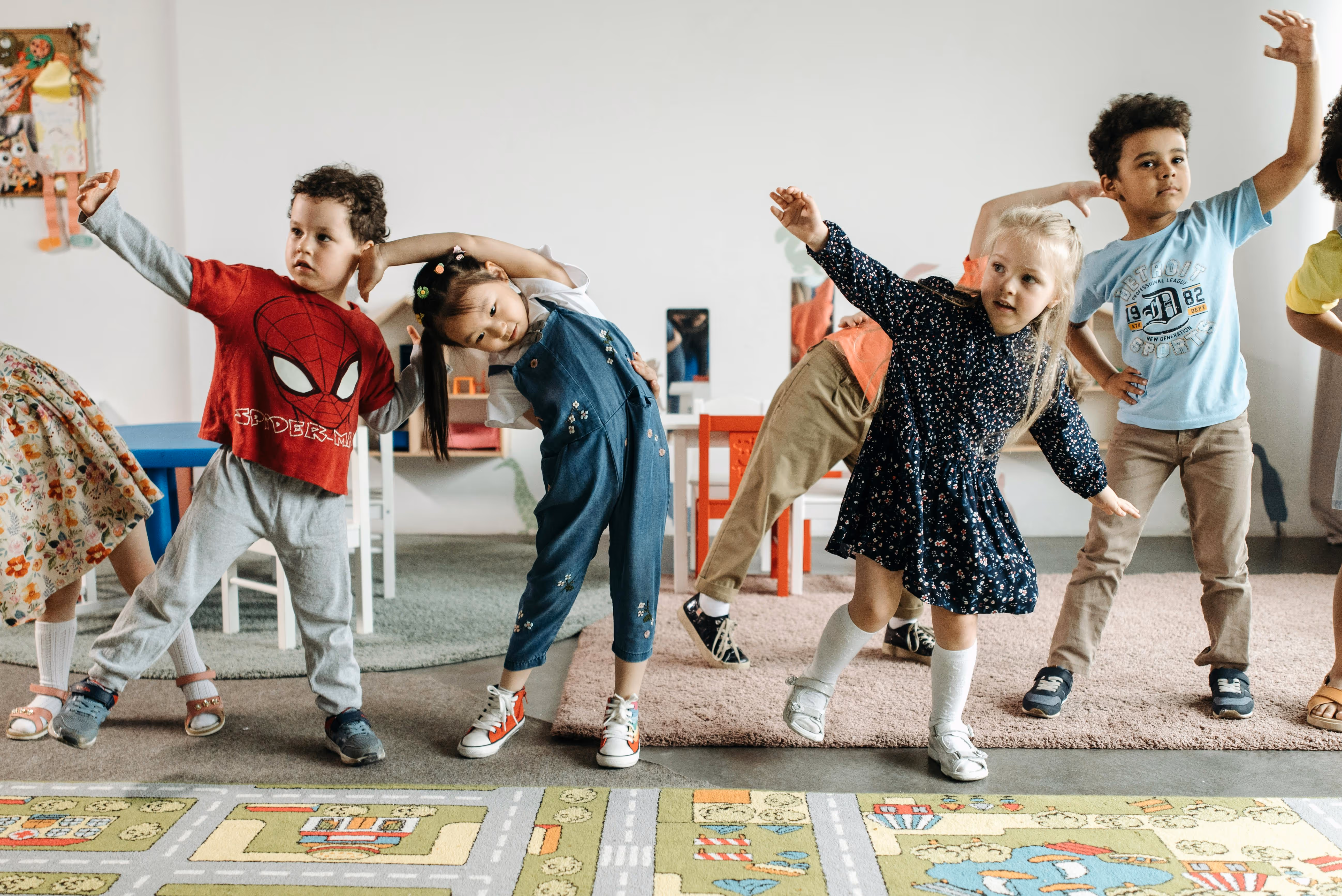 Group of young children in casual clothes stretching and exercising together in a classroom.