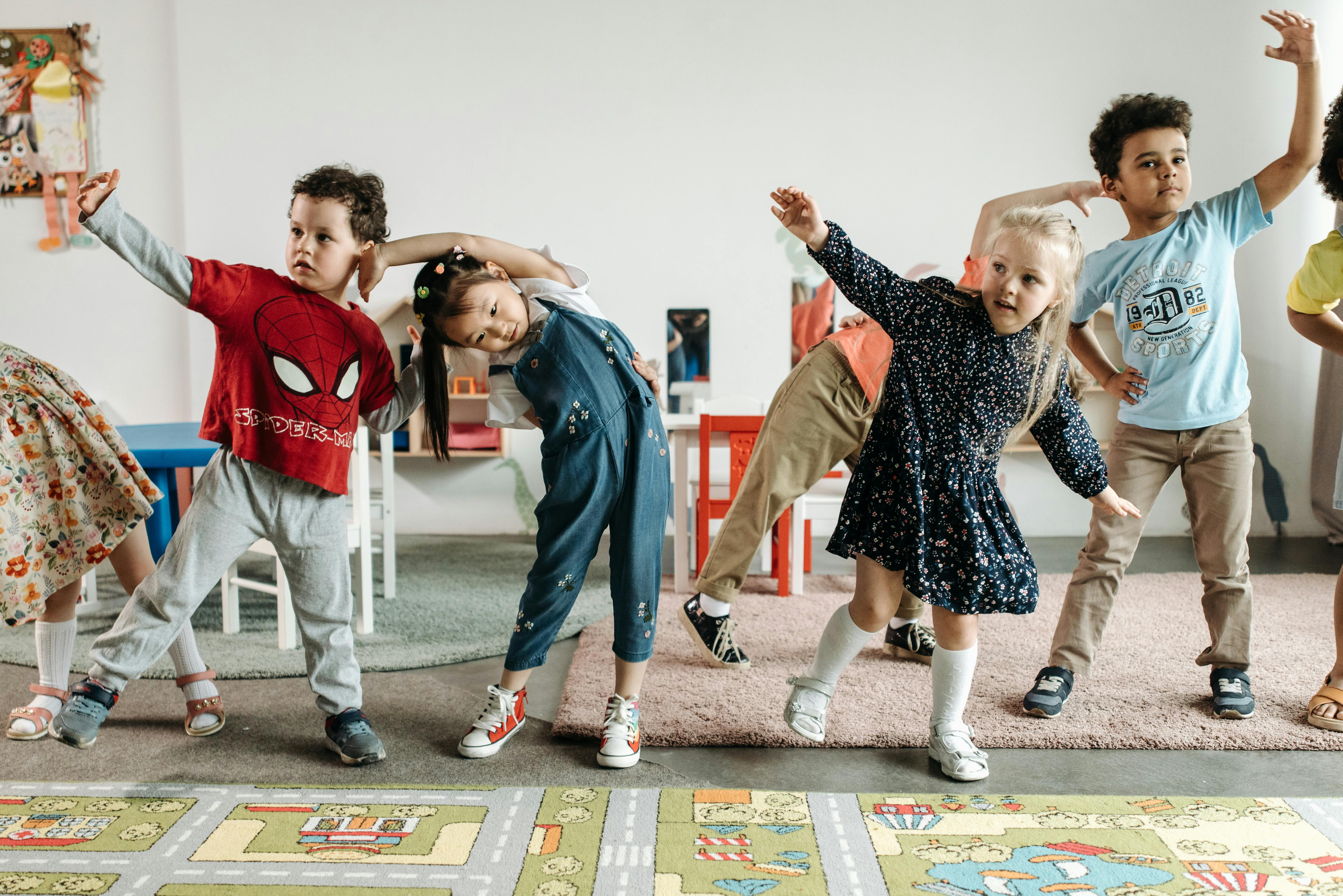 Group of young children in casual clothes stretching and exercising together in a classroom.