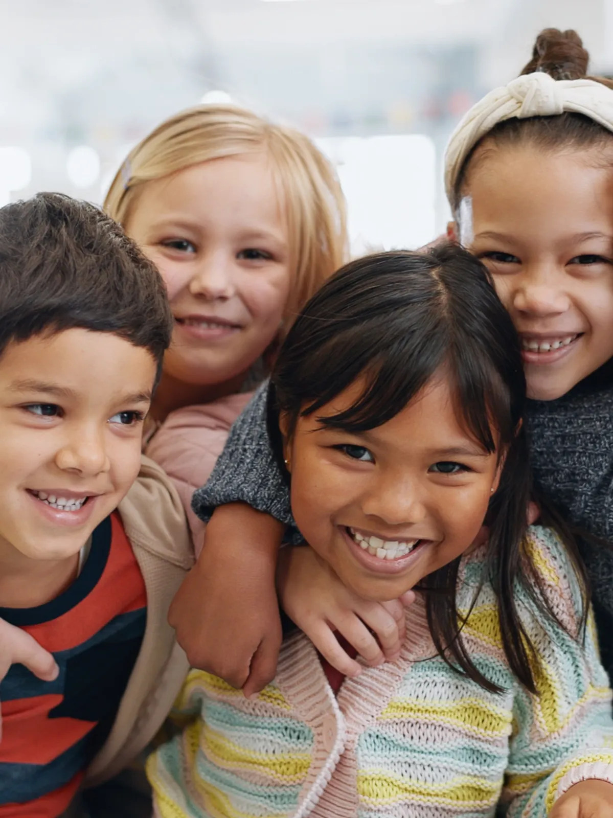 Four smiling children closely grouped together indoors, showing friendship and happiness.