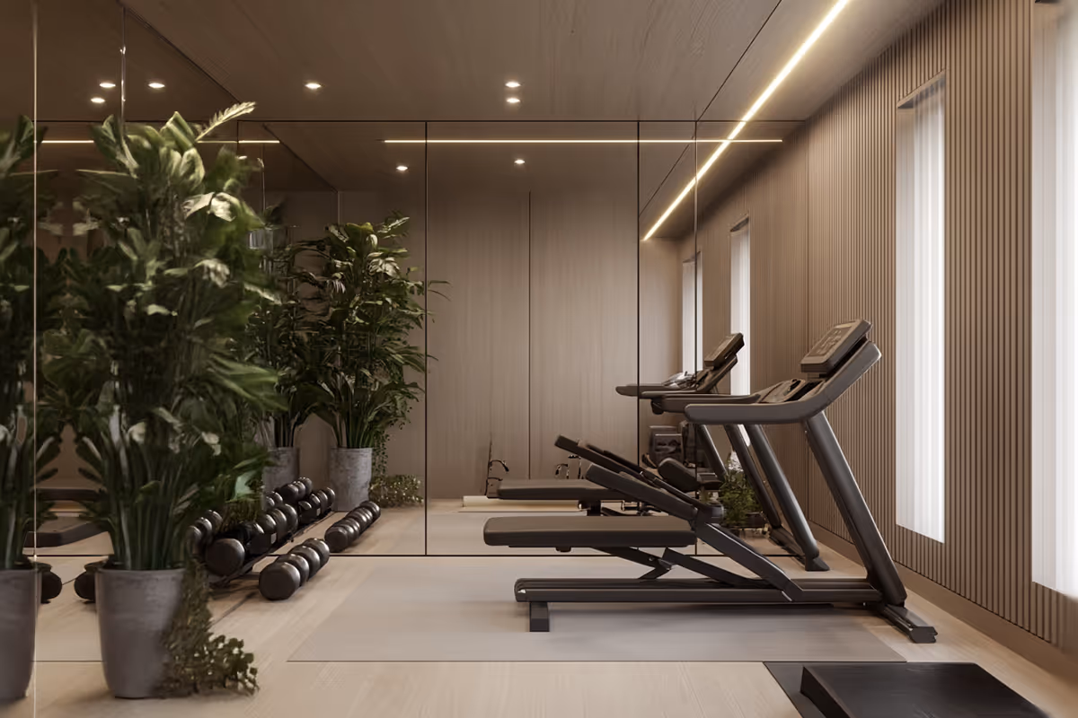 Modern gym room with two treadmills, dumbbells on the floor, and large green plants against mirrored walls.