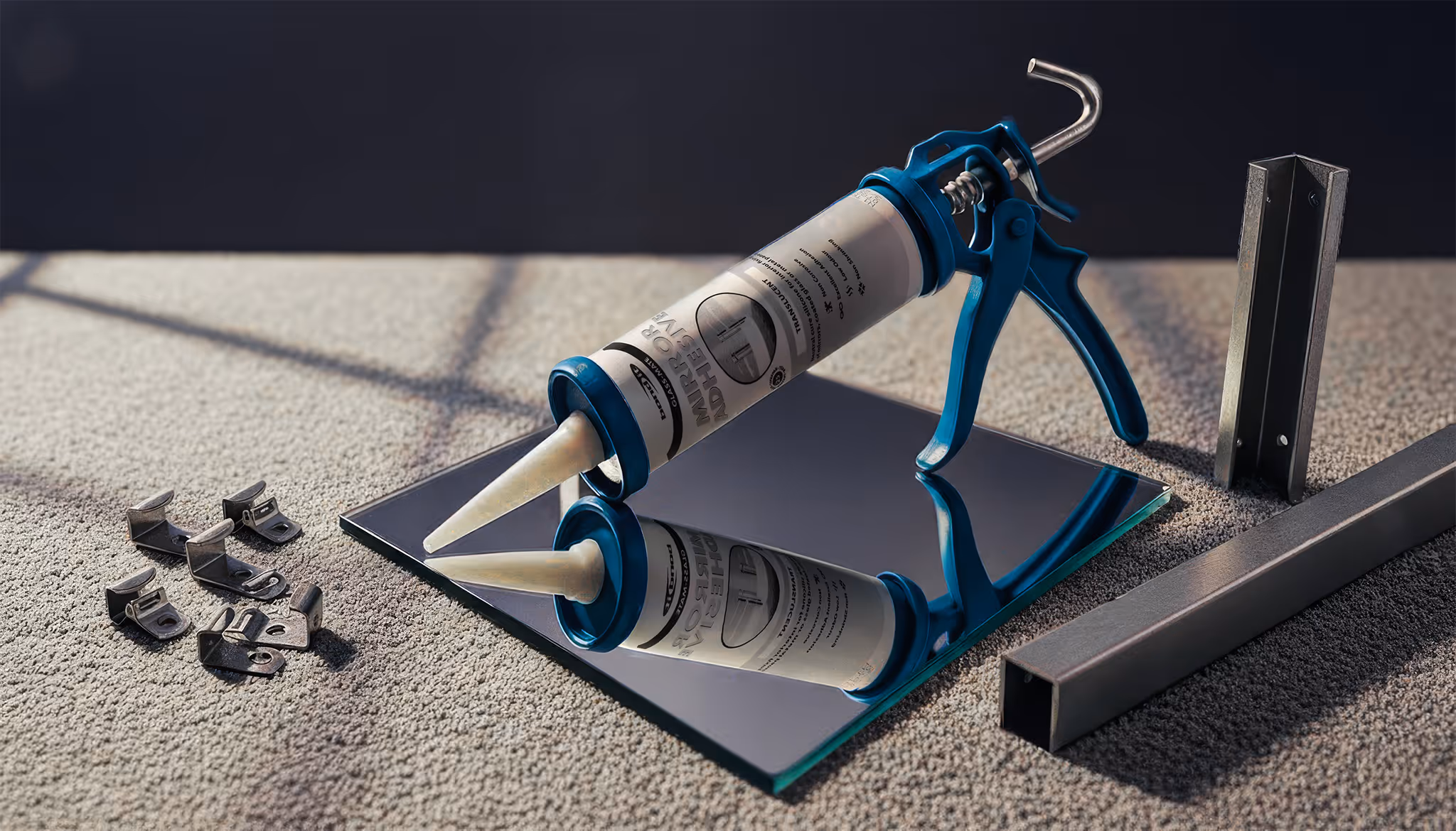 Caulking gun with tube of transparent adhesive resting on a reflective glass surface, surrounded by metal brackets on carpet.