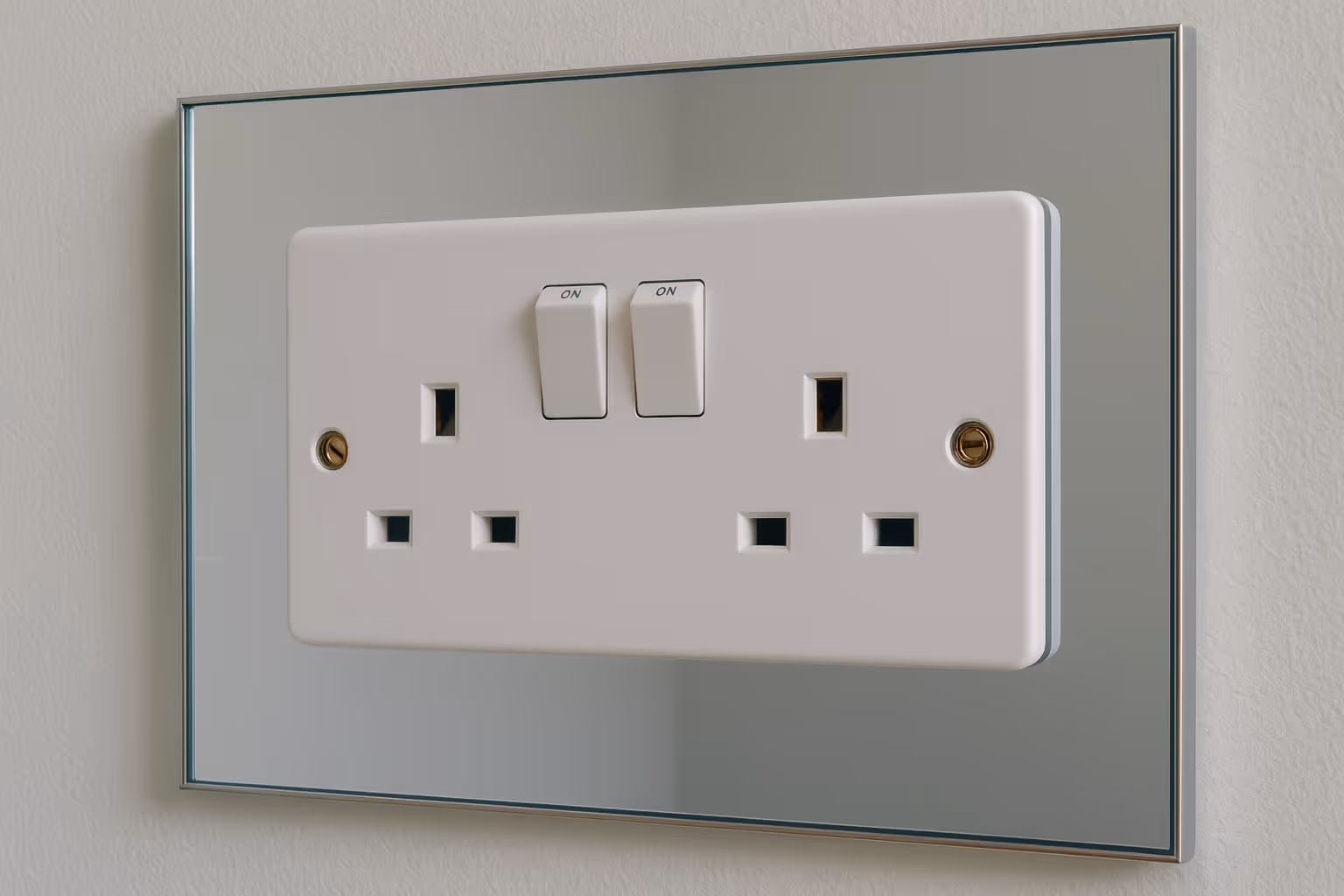 A close-up of a white double UK plug socket with two switches, mounted onto a mirrored wall plate. The mirror reflects the socket edges and is framed with a thin metallic border, set against a light grey wall.
