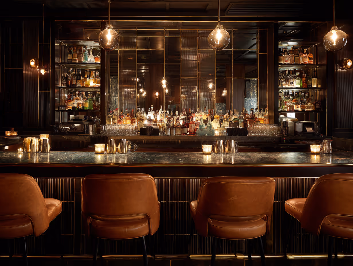 Luxurious cocktail bar with brown leather stools, a marble countertop, and a fully stocked mirrored back wall under warm lighting.