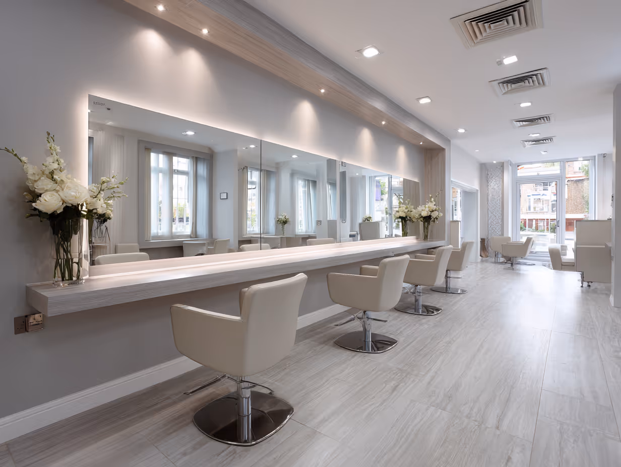 Bright, modern hair salon with cream-colored styling chairs, large wall mirror, and white floral arrangements.
