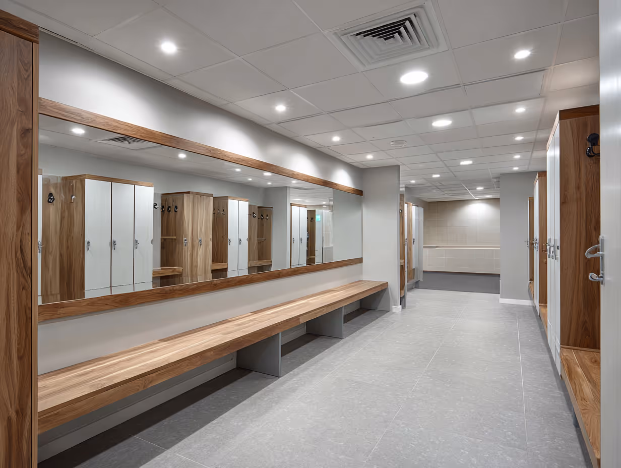 Modern staff changing room with wooden lockers, a long wooden bench, large wall mirror, and recessed ceiling lights.
