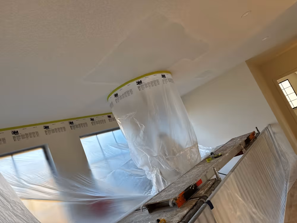 Interior of a room with plastic sheeting covering furniture and windows, and a plastic containment tent sealed to the ceiling for renovation work.