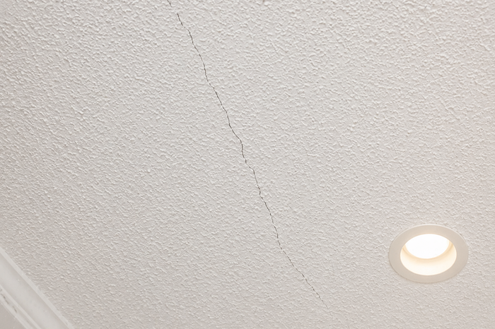 White textured ceiling with a visible long crack running diagonally and a round recessed light fixture on the right.