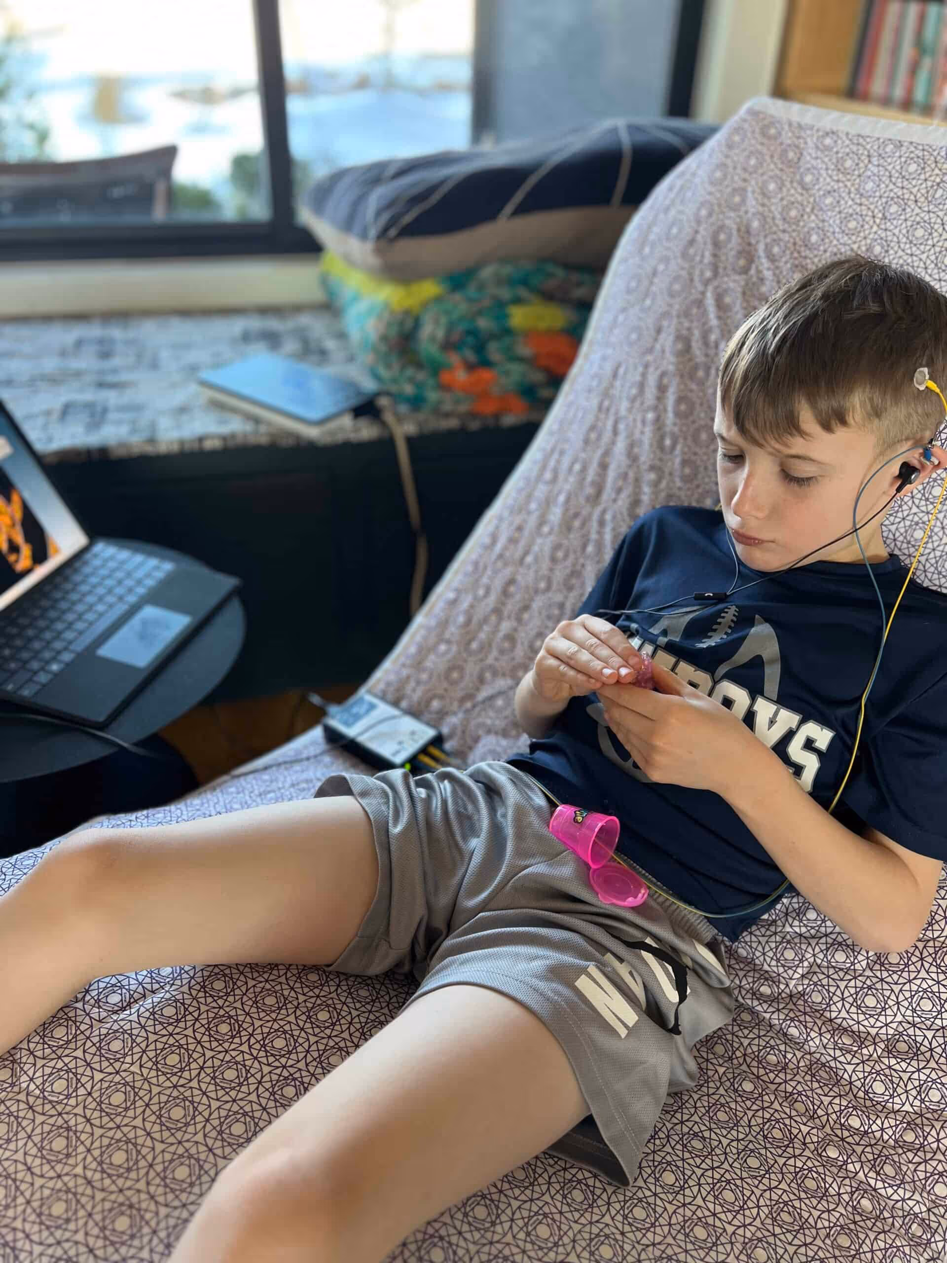 Young boy wearing earphones reading a blue book titled 'Coup Soleil' while sitting on a couch.