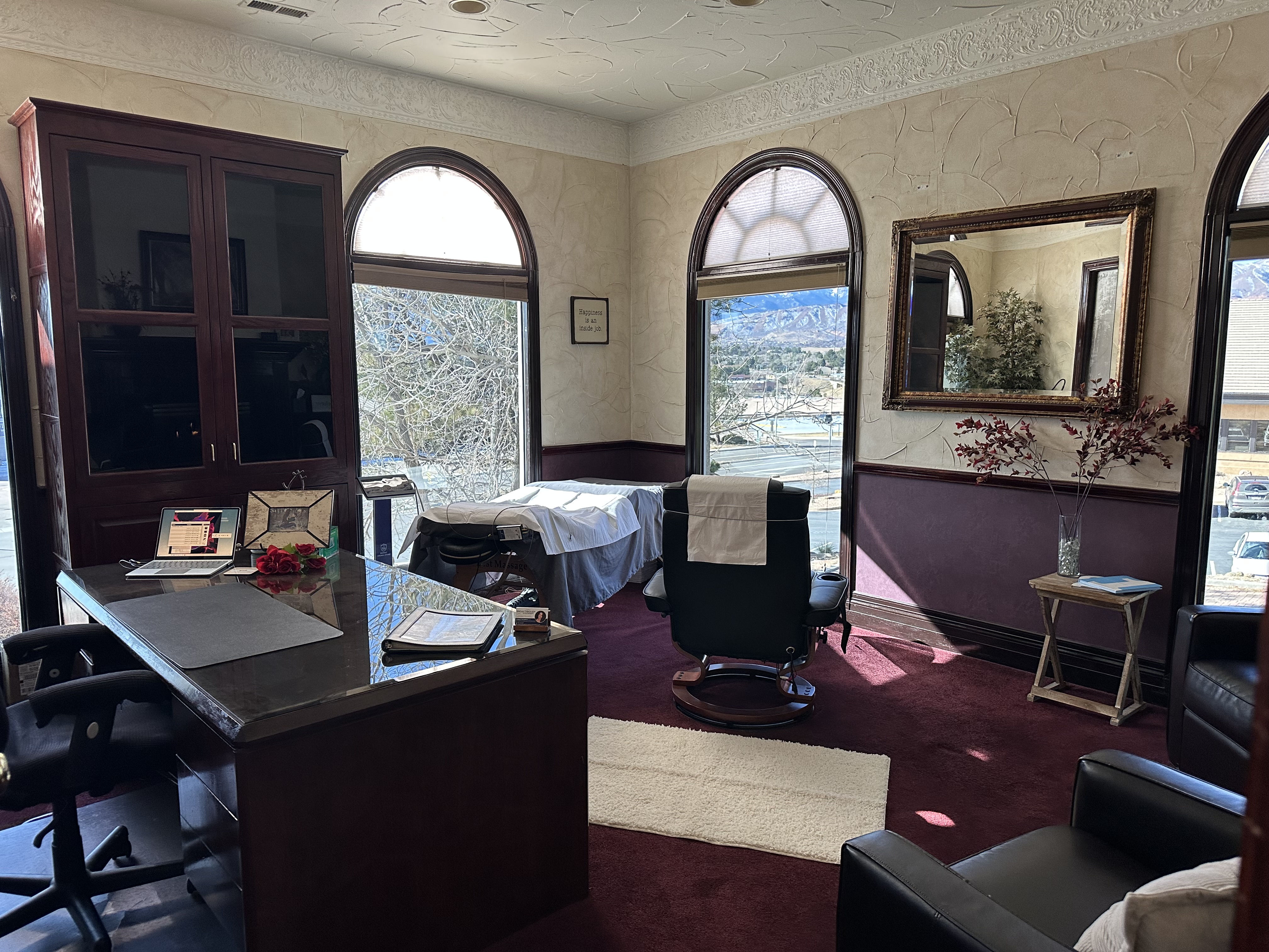 Cozy living room with dark leather chairs, a fireplace, decorative pillows, and floral arrangements near a large window with curtains.