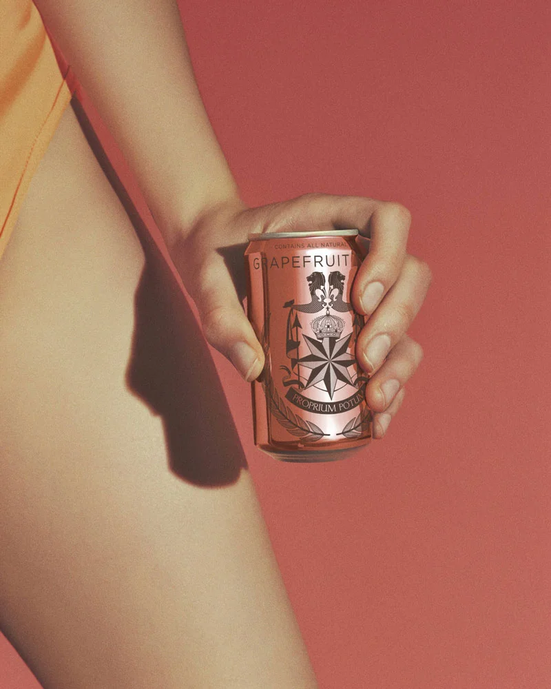 Hand holding a pink grapefruit tonic soda can against a coral background with part of an arm visible.